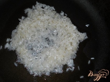 В сковороду налить растительное масло, прогреть. Рис помыть несколько раз до прозрачности воды. Высыпать в сковороду. Перемешать и обжарить минуты 3.