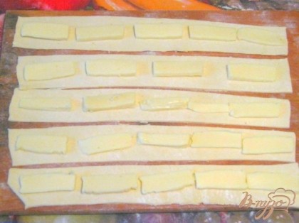 Плавленный сыр нарезать ломтиками и выложить посередине каждой полоски слоеного теста. Затем тесто аккуратно сложить вдвое и защипать края по всей длине полоски.
