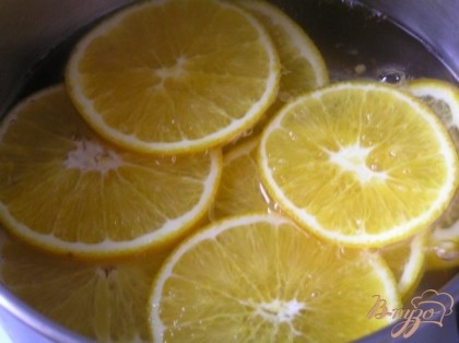 Приготовить декор-начинку. Вскипятить воду, добавить сахар и перемешать до растворения, добавить нарезанные тонкими ломтиками апельсины, варить 10-12 минут