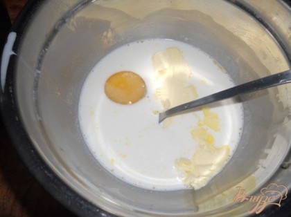 В другую миску к сливкам перемешанным с водой, добавить сахар, яйцо, 70 г размягченного сливочного масла и хорошо перемешать.
