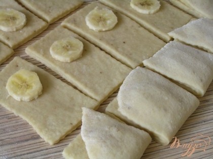 Затем раскатать тесто в пласт, нарезать на прямоугольники. Оставшуюся половинку банана нарезать на кружочки. На каждый прямоугольник положить по кружочку банана и свернуть пополам.