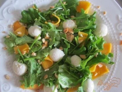 На тарелочки выложить листья салата, сыр и полоски манго, покрошить орешки.