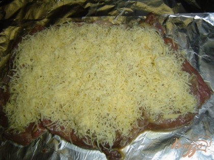 Достаем мясо из маринада, выкладываем его на фольгу, смазываем горчицей и посыпаем натертым сыром.