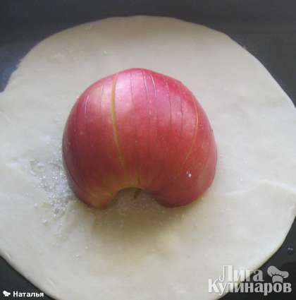 Готовим начинку из яблок,  сорт можно брать любой, но лучше кисло-сладкий. Режем яблоко на две половинки, вырезаем сердцевину, и делаем вертикальные надрезы по всему яблоку. На кружочек теста, посыпанного сахаром кладем  половинку яблока, надрезами вверх.