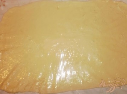 После того как тесто подошло и увеличилось в размере, раскатываем его в пласт и смазываем поверхность маслом.