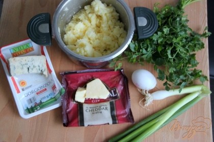 Отварить картофель и размять его, как на пюре. Подготовить другие продукты. Измельчить лук и зелень. Сыр нарезать мелкими кубиками или натереть.