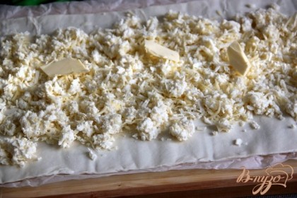 Раскатать на противне, на бумаге для выпечки пласт слоёного теста, посыпать 1/3 сыра и пластинками сливочного масла.
