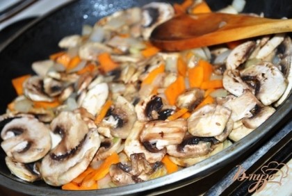 К луку с морковью добавьте шампиньоны, нарезаные пластинками. Обжаривайте, пока не выпарится жидкость, которую пустят грибы.