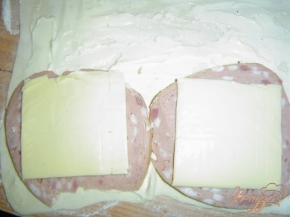 Кусочки колбасы покрываем тонкими ломтиками плавленого сыра.