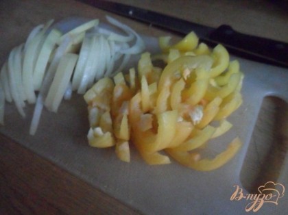 Тем временем вымыть овощи, очистить. У перца удалить сердцевину. Лук нарезать полукольцами. Полукольцами нарезать болгарский перец.