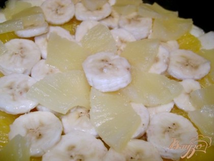 Нарезать банан кольцами, яблоко пластинами, апельсин дольками, кольца ананаса на четыре части. Отдельно взбить яйцо, оставшийся сахар, сметану до гладкого крема. Разъёмную форму смазать маслом, выложить тесто, на него фрукты,