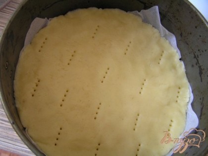 Форму для выпечки застелить пекарской бумагой, распределить тесто, проколоть вилкой в нескольких местах.