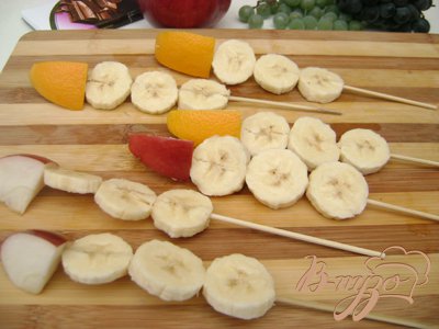 На деревянные шпажки одеть по три кусочка банана, и по кусочку яблока или апельсина. Из цедры апельсина вырезать «носики». Вставить «носики» в первый кусочек банана. Шоколад растопить. Нарисовать им при помощи спичек глаза и пуговицы.