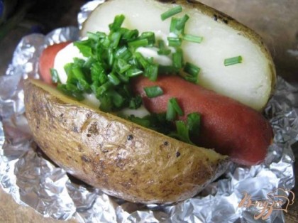 В разрезанный картофель кладём ложку сметаны (йогурта или майонеза), посыпаем зеленью, зелёным луком. Любители могут добавить кетчуп. А сверху кладём запечённую сосиску.