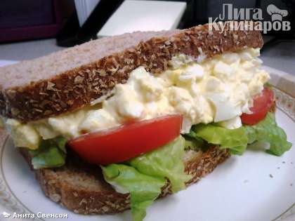 На подсушенный или поджаренный хлеб выкладываем лист салата, пару долек помидора и 1/2 начинки, прижимаем вторым куском хлеба. Также поступаем со 2ым сэндвичем.