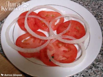 Укладываем на тарелку несколько кружков помидора, затем несколько колец лука