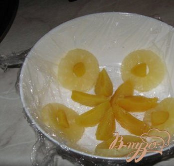 Взять большую миску или салатницу. Выстелить ее пищевой пленкой так, чтоб края ее свисали. На дно выложить ананасы и персики.