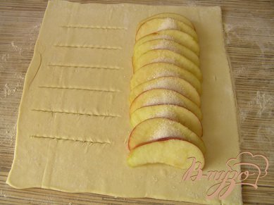 С одной стороны каждой части выложить нарезанное дольками яблоко, посыпать сахаром, с другой следать надрезы с интервалом 1,5-2 см.
