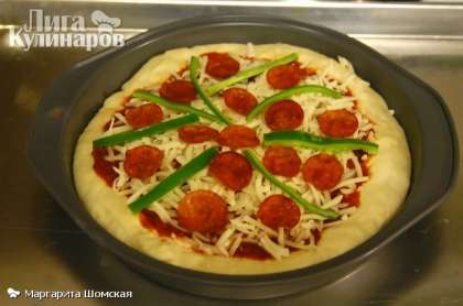 Увеличиваем температуру в духовке до 200 °. Покрываем пиццу соусом. Далее посыпаем пиццу  1 стаканом тертого сыра затем добавляем начинку по своему выбору (например, пепперони и перчики чили).