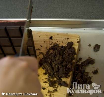 Разрежьте шоколад на кусочки  с помощью большого зазубренного ножа. Так как при нарезании шоколада ножом, кусочки шоколада будут лететь в разные стороны, то лучше всего это делать на противене с высокими краями.