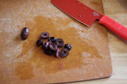 Сначала нам нужно подготовить все ингредиенты. Открываем оливки или маслины, сливаем с них рассол и выкладываем на разделочную  доску. Нарезаем их маленькими кусочками.