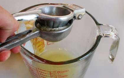 Переложить на разделочную доску очищенный от шкуры лимон и разрезать его пополам. Выдавить, воспользовавшись ручной соковыжималкой, сок из каждой половинки лимона. Перелить сок в отдельную чашку.