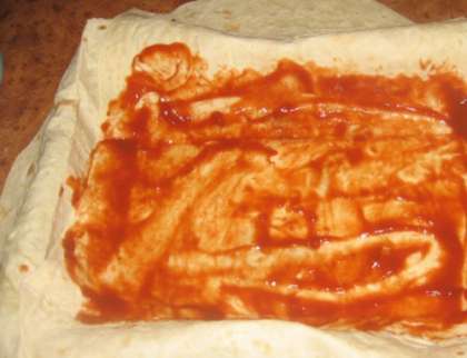 После этого промазать по всему периметру листы томатным соусом. Сверху уложить равномерно ветчину. Затем слой огурцов. Теперь нужно смазать все майонезом. Засыпать сверху  тертым сыром и накрыть висящими краями верхнего лаваша.