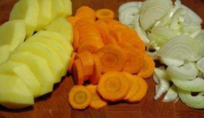 Картофель, морковь и лук промойте, очистите и нарежьте небольшими кубиками. Зелень измельчите.