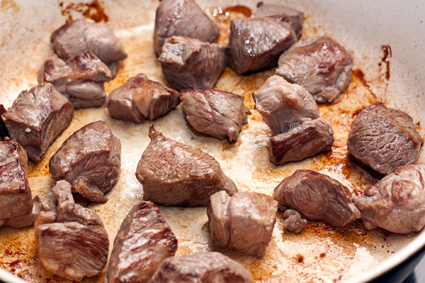 Мясо, подходящее для тушения, зачистите от жил и лишнего жира, нарежьте кубиками примерно 2 см.  Обжарьте небольшими порциями без масла на хорошо разогретой сковороде.