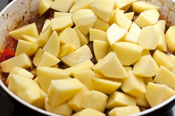 Пока тушится мясо, очистите и нарежьте картофель также, как баранину. Положите его в сковороду, перемешайте. накройте крышкой и тушите еще полчаса до мягкости. 