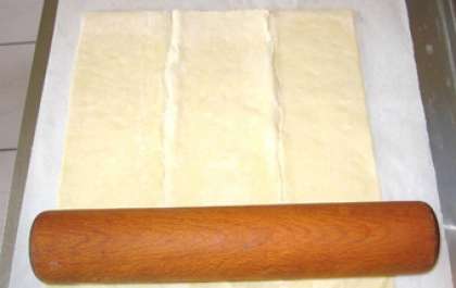 Для  этого пирога будем использовать готовое слоеное тесто. Заранее достанем из морозильника тесто, чтобы оно разморозилось. Затем на кухонном столе, покрытом пергаментной бумагой, раскатать тесто в пласт и, придерживая края бумаги, переложить на противень.