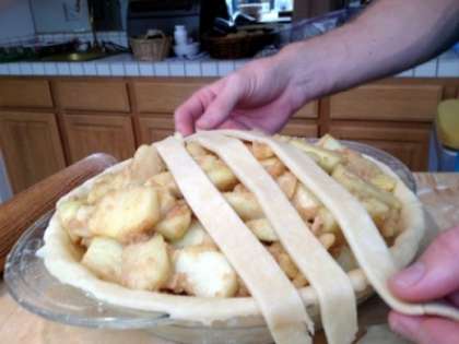 На сформированную основу для пирога в форму для выпекания выложить яблочную начинку. Достать из холодильника тесто, что осталось. На рабочую поверхность стола, присыпанного мукой, положить шар теста и раскатать его пластом толщиной  4 миллиметра. Разрезать пласт на полоски шириной сантиметра  два и уложить на поверхность пирога так, как показано на фото. Сформировать из полосок плетение.