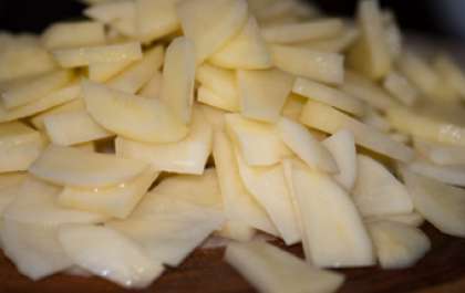 Для начала подготовим картофель. Вымыть его и очистить от кожуры. Переложить на разделочную доску корнеплоды. С помощью ножа разрезать картофель на тонкие пластинки. От толщины картофельных пластинок зависит время приготовления блюда.