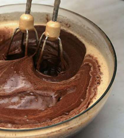 Растворенный шоколад с маслом добавляем к золотисто-коричневой массе и размешиваем при помощи миксера. После этого добавляем муку и снова размешиваем до однородной массы. Шоколадную смесь посолим и опять размешаем миксером.