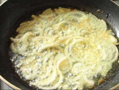 На другой сковороде обжариваем нашинкованную кольцами луковицу до тех пор, пока она не станет золотистого цвета.