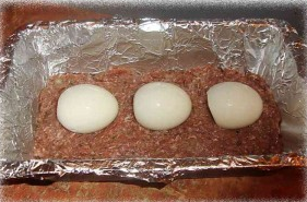 По центру фарша аккуратно разложить вареные яйца (яйца можно разрезать пополам и выложить половинками, тогда в разрезе рулет будет выглядеть немного по-другому).