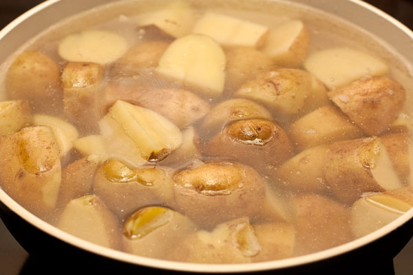 Тщательно вымойте картофель с щеткой, разрежьте каждую картофелину на 2-6 частей в зависимости от исходного размера и положите в глубокую сковороду с толстым дном. Залейте кипящей водой так, чтобы она покрыла картофель.