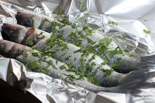 Разложите рыбу на противне, застеленном фольгой и смазанном маслом.  Сверху рыбу смажьте маслом, слегка посолите и присыпьте оставшейся зеленью.