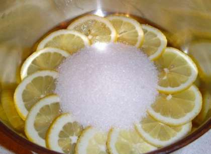В кастрюлю или другую емкость (с широким дном: миска, тазик) насыпьте сахара и добавьте воды (небольшое количество, хватит и полстакана стакана, может чуть больше). Готовьте лимонные дольки на небольшом огне минут десять, периодически помешивая лимон в сиропе деревянной ложечкой.