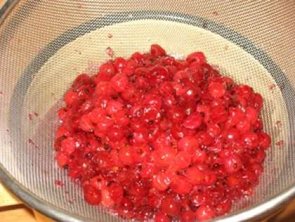 Обычно когда ягоды красной смородины подвергнуть варке, она потеряет свой цвет и вид. Поэтому процедите готовое варенье в отдельную посуду. Собранную ягоду протрите через сито, чтобы максимально использовать самое вкусное и полезное. Затем выложите массу в сироп и перемешайте.