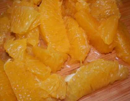Далее разделите апельсин на дольки. Потом апельсиновые дольки разрежьте пополам. Оставьте только мякоть. Сложите их в емкость и разомните пестиком или ложечкой, пока они не пустят сок.