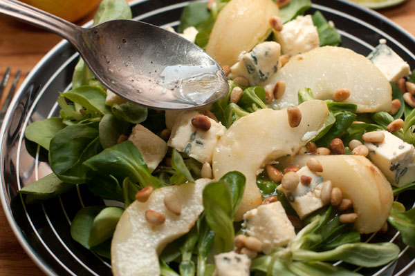 На листья салата выложите груши, нарезанный кубиками сыр, посыпьте орешками и полейте заправкой.