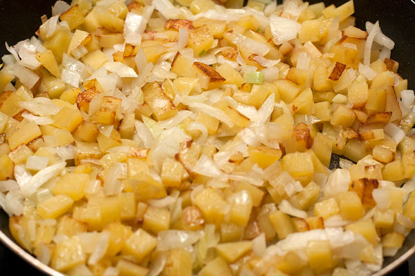 Лук нарежьте не слишком мелко и поджарьте до легкого золотистого цвета. Очищенную картошку можно натереть на крупной терке или нарезать мелкими кубиками, а затем добавить к луку.