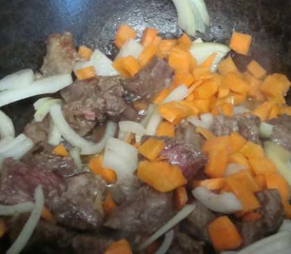 Как только мясо зарумяниться, добавьте нарезанную морковь и лук кусочками. Также налейте в казан необходимое количество воды. Продолжайте тушить мясо с луком.