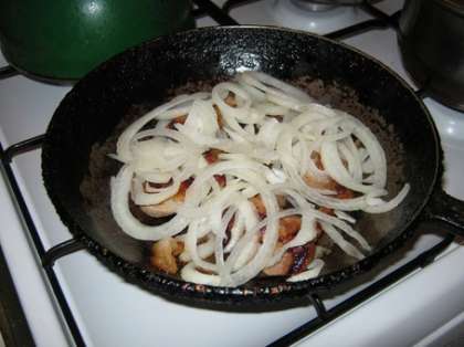 Когда мясо покроется жареной корочкой с одной стороны, переверните его на другую сторону и добавьте между кусочками подготовленное ранее сало. Затем выложите поверх мяса порезанный лук и накройте сковороду крышкой.
