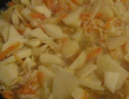 Приготовьте глубокую емкость. Выложите порезанный картофель, далее добавьте морковь и нашинкованную капусту. Положите размягченное масло в посуду. Перемешайте. Затем киньте чеснок и измельченный чеснок. Посолите ваше блюдо, можно также бросить специи. Влейте в емкость с овощами  воды. Количество жидкости должно не доходить до уровня овощей на 1-2 см. Накройте емкость крышкой, и поставьте на огонь (медленный). Тушите картофель с овощами около получаса.