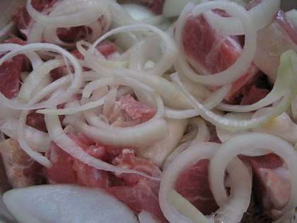Нарезанное мясо нужно уложить в глубокую кастрюлю. Туда также добавить предварительно нарезанный лук, хорошо все перемешать и помять мясо с луком, чтобы лук стал менее жестким, а мясо стало мягким.