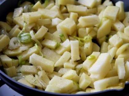 Картофель нарежьте средними кубиками и выложите в сковороду к чесноку и луку.