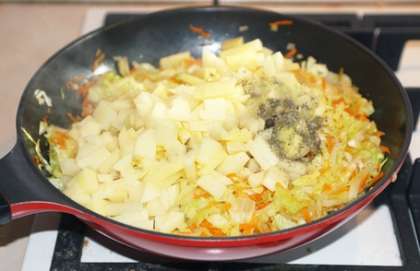 Когда капуста размягчится и будет хрустящей, добавьте к ней картошку, сушеный базилик и черный перец горошком. Также влейте полстакана воды, перемешайте, закройте крышкой и тушите на небольшом огне до готовности картошки.
