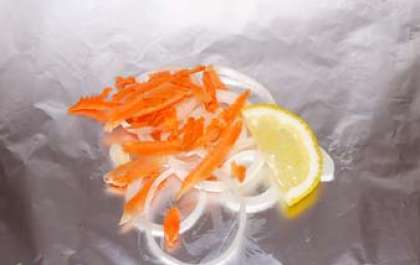 Отрежьте кусочек фольги. Смажьте ее маслом растительным. Положите на него немного лука, моркови и лимон.